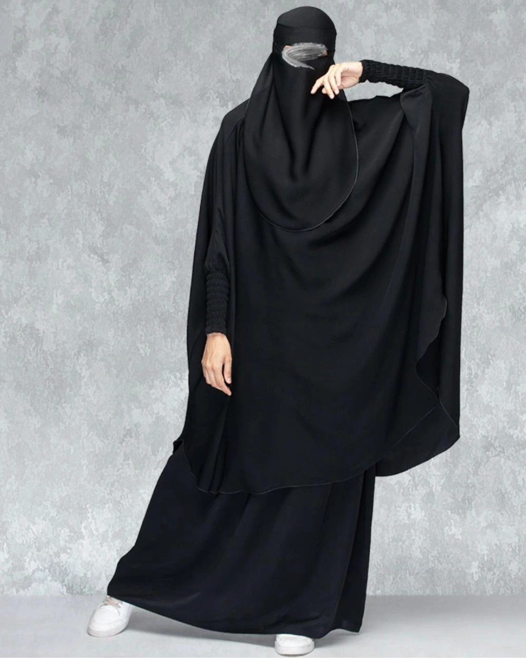 Detaillierte Ansicht des 3-teiligen Jilbab-Set in Schwarz, durch einen gehobenen Arm sieht man deutlich den weiten Khimar, Rock, Niqab und die detailreichen, strukturierten Ärmelbündchen. In Einheitsgröße passend für kleine und große Frauen. 