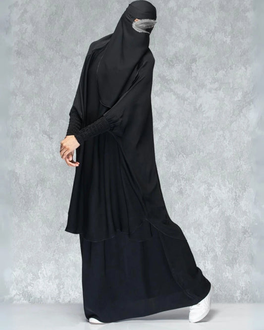 Detaillierte Ansicht des 3-teiligen Jilbab-Set in Schwarz von der Seite mit weitem Khimar, Rock, Niqab und detailreichen, strukturierten Ärmelbündchen. In Einheitsgröße passend für kleine und große Frauen. 